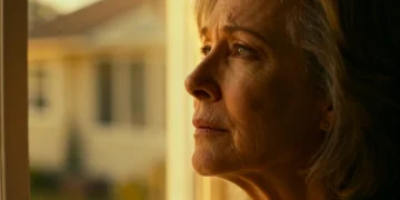 Femme pensive regardant par la fenêtre, symbolisant la réflexion sur l'allocation de veuvage.